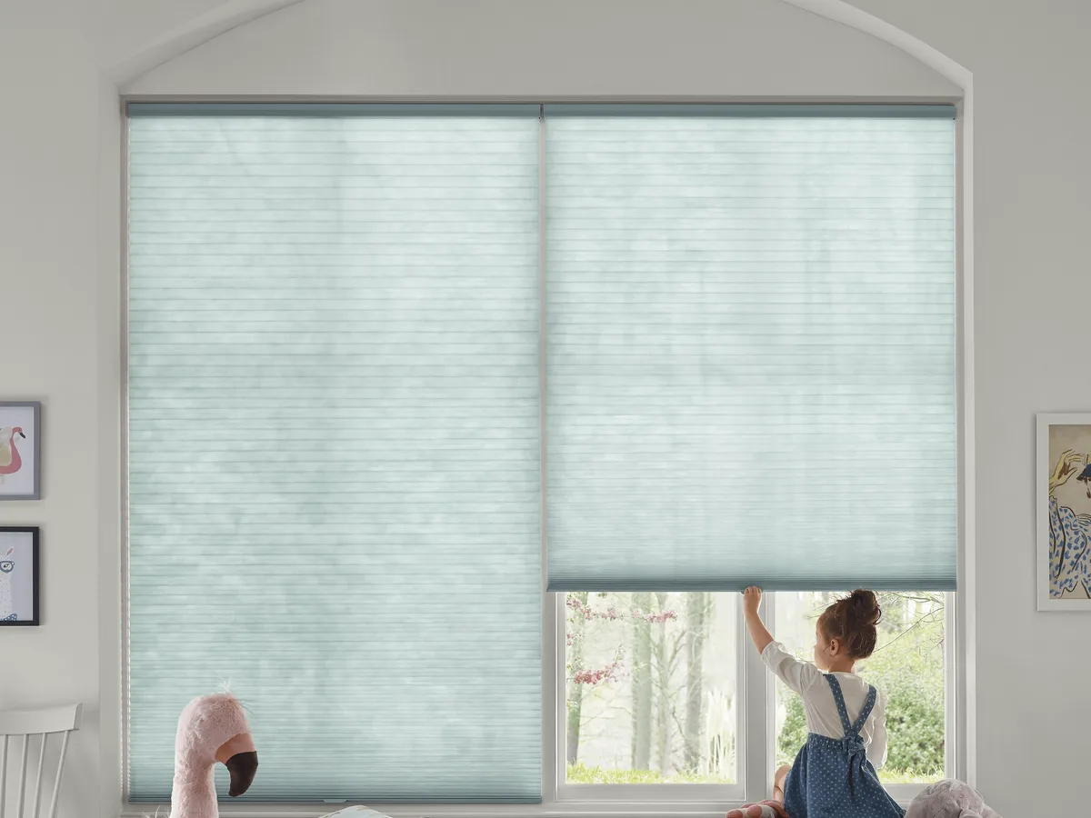 Hunter Douglas Applause honeycomb shades on an arched child&rsquo;s-room window, one shade raised to show the view and the honeycomb cells lit from behind