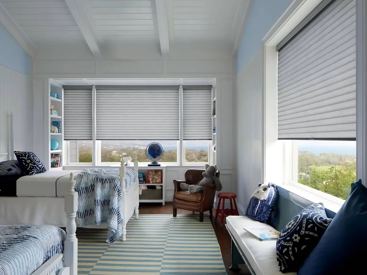 Hunter Douglas Sonnette cellular roller shades in a coastal bedroom, the curved cells catching the light with the ocean beyond