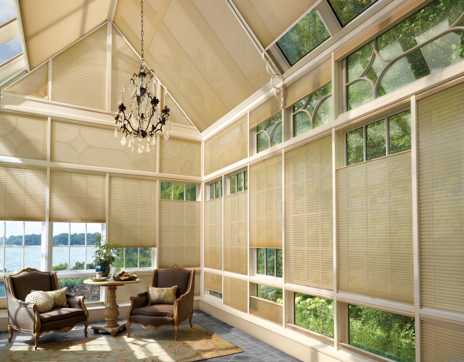 Sunroom with a sloped glass ceiling and window walls fitted with honeycomb shades, overlooking the water