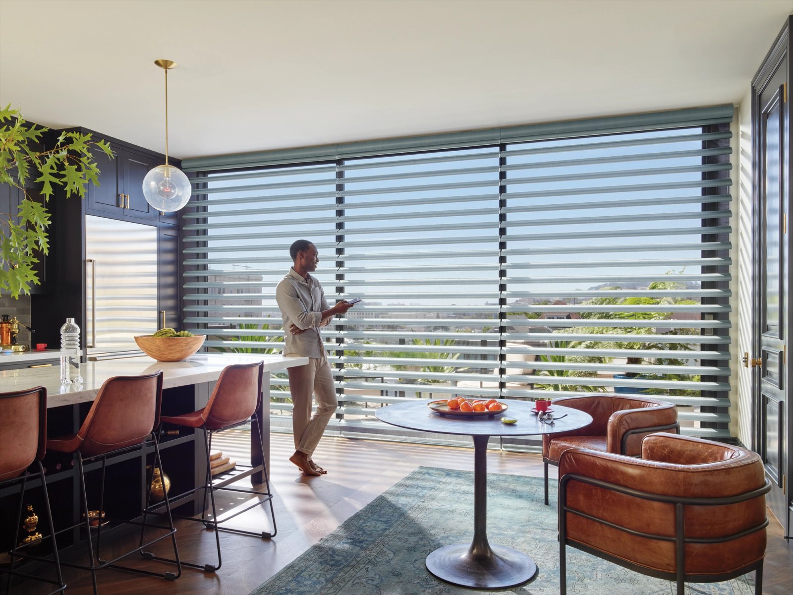 Homeowner raising motorized shades from a tablet in an open-plan living room